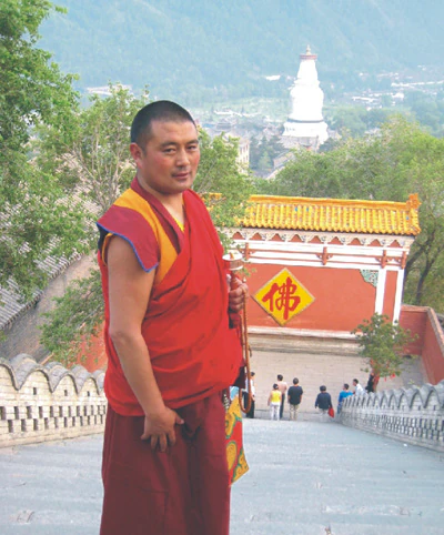 Hor shul Khenpo Gelek Palsang Rinpoche stands in monastic robes on stone steps at Tayuan Temple on Mount Wutai, with a white stupa in the distance.