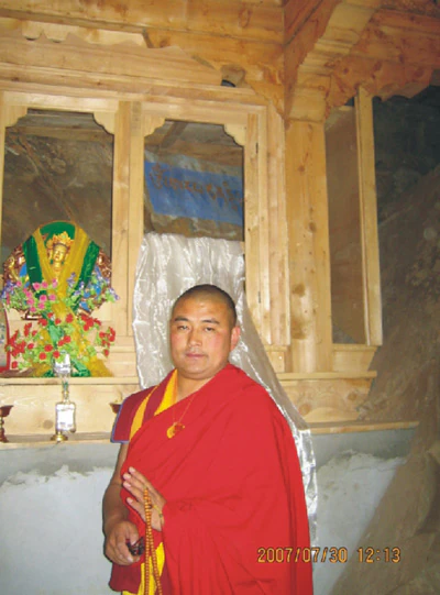 Hor shul Khenpo Gelek Palsang Rinpoche stands in monastic robes beside a religious relic enclosed by wooden railings.