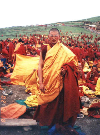 Hor shul Khenpo Gelek Palsang Rinpoche stands in yellow ceremonial robes before a large monastic gathering at a Kalachakra empowerment at Larung Gar Five Sciences Buddhist Institute.