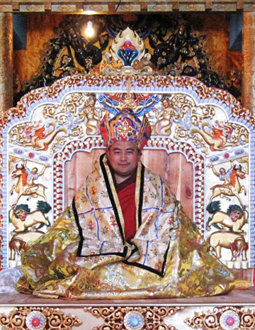 Hor shul Khenpo Gelek Palsang Rinpoche sits on an ornate ceremonial seat wearing ritual robes and a ceremonial hat.