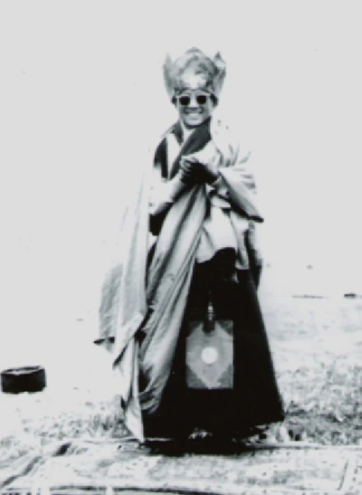 In a faded black-and-white photograph, eleven-year-old Hor shul Khenpo Gelek Palsang Rinpoche stands outdoors wearing dark glasses and holding an object in both hands.