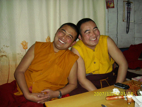 Hor shul Khenpo Gelek Palsang Rinpoche and Tulku Tudeng Longduo smile side by side indoors in yellow and red robes.