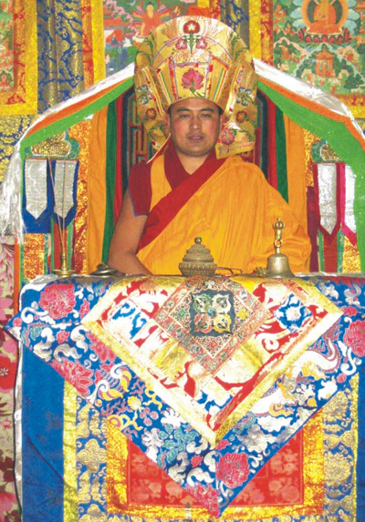 Hor shul Khenpo Gelek Palsang Rinpoche sits on a painted ceremonial seat wearing ritual robes and a ceremonial hat.