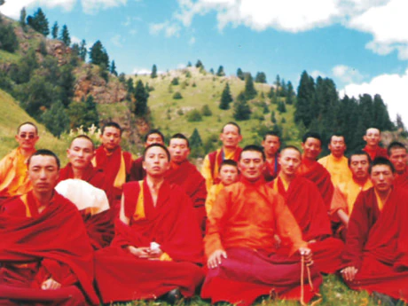 Hor shul Khenpo Gelek Palsang Rinpoche and students of the tulku class at Larung Gar Five Sciences Buddhist Institute pose together on a wooded grassy slope in red robes.