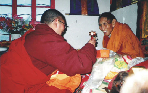 Sangjie Danzeng Rinpoche and Hor shul Khenpo Gelek Palsang Rinpoche speak together indoors in monastic robes.