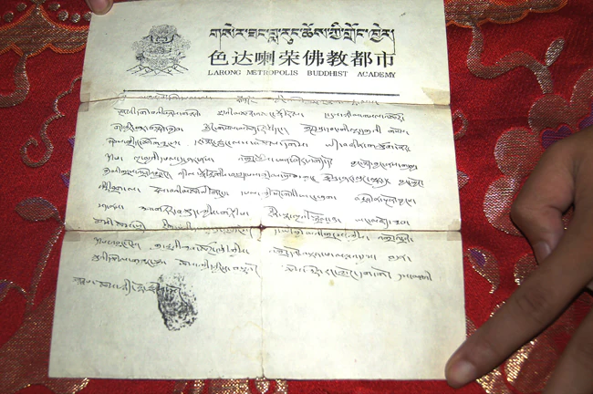 A handwritten Tibetan prophecy document with a printed letterhead and seal rests on red patterned brocade.