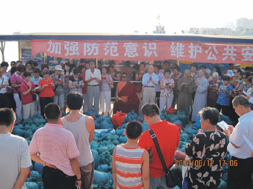 Hor shul Khenpo Gelek Palsang Rinpoche and a crowd stand before stacks of blue bags containing aquatic animals during a life-release event in a Han Chinese area.