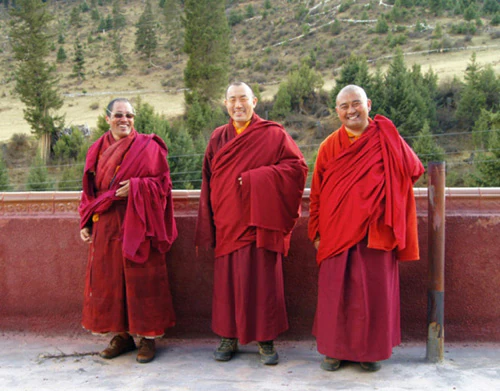 Hor shul Khenpo Gelek Palsang Rinpoche, his maternal uncle Khenpo Qiupeng, and another monastic pose outdoors in red robes.