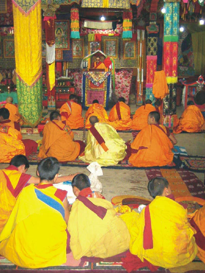 Hor shul Khenpo Gelek Palsang Rinpoche teaches from a ceremonial seat in the shrine hall of Hor shul Monastery while monastics sit facing him.