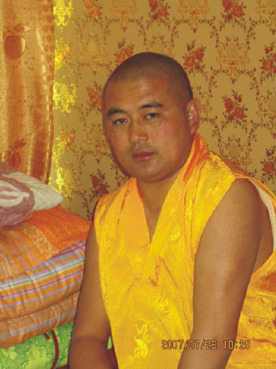 Hor shul Khenpo Gelek Palsang Rinpoche sits indoors wearing yellow ceremonial robes.