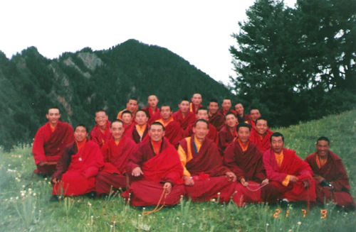 Hor shul Khenpo Gelek Palsang Rinpoche and students of the tulku class at Larung Gar Five Sciences Buddhist Institute pose together on grass in red robes.